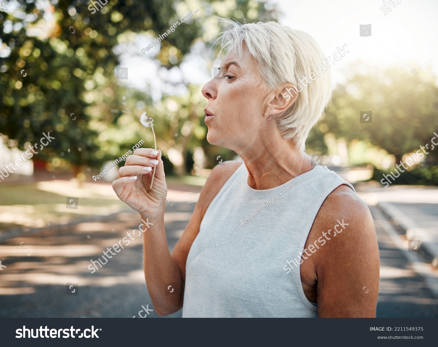 Senior woman blowing dandelion flower outdoors for freedom, hope and spring allergies environment. Elderly retirement lady holding plant for wellness, healthy lifestyle and pollen allergy in nature #2211549375