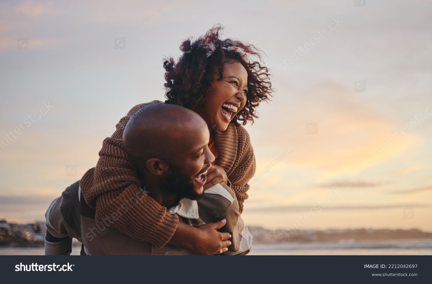 Black couple, travel and beach fun while laughing on sunset nature adventure and summer vacation or honeymoon with a piggy back ride. Comic, energy and black man and woman love on ocean holiday #2212042697
