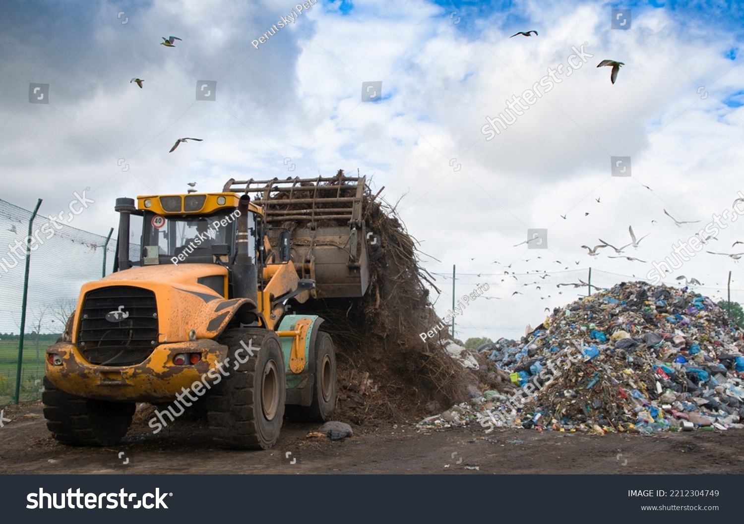 bulldozer working on landfill with birds in the sky #2212304749