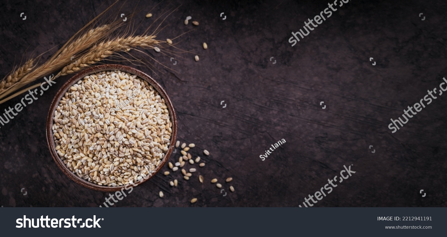 Bowl of dry raw broken pearl barley cereal grain on dark background. Cooking pearl barley porridge concept. #2212941191
