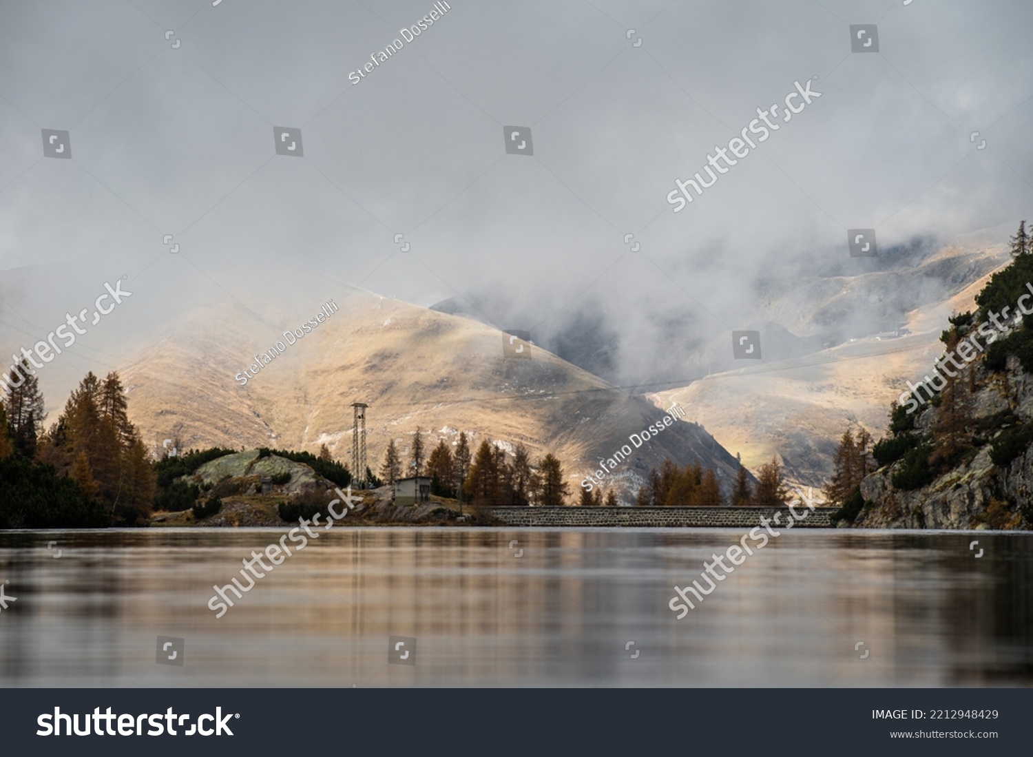 Low angle shot from the surface of the water of Lago Marcio, with orange hills and low clouds in the background, Northern Italy #2212948429