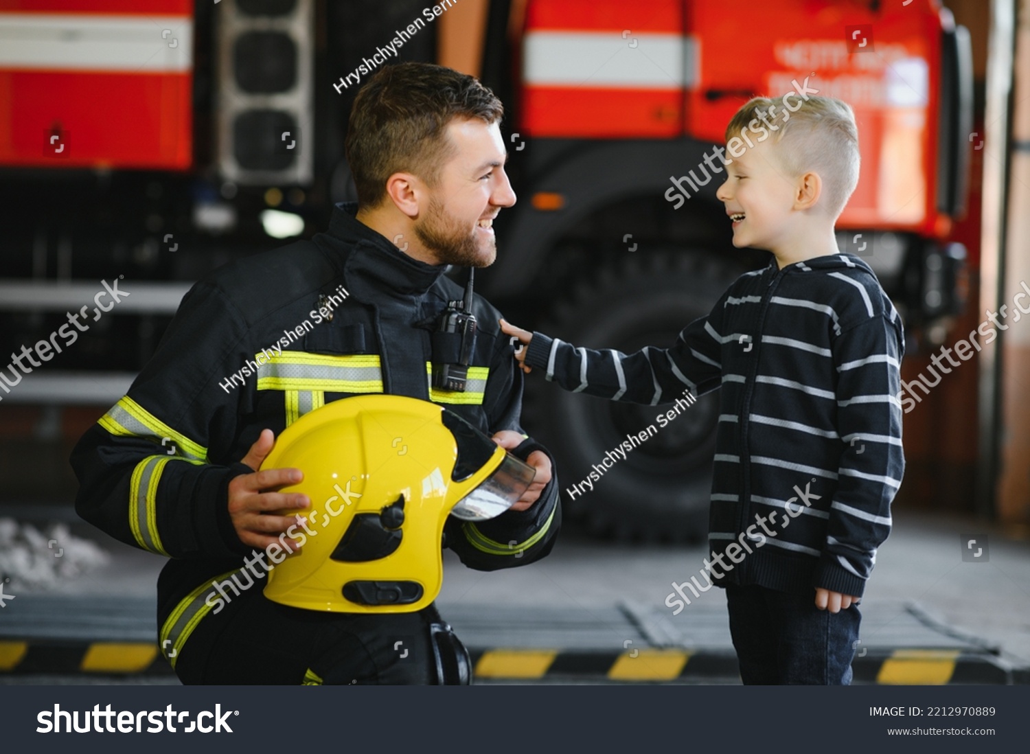A firefighter take a little child boy to save him. Fire engine car on background. Fireman with kid in his arms. Protection concept #2212970889