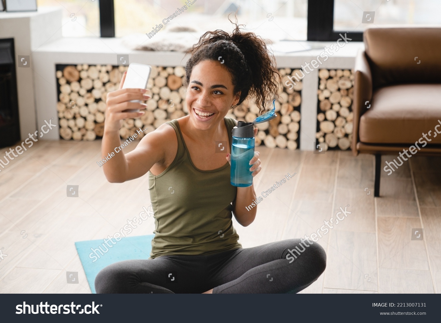 Home workout. Online vlogging blogging training on fitness mat using cellphone. African young female athlete doing yoga exercises at home, having videocall, video tutorial, taking selfie #2213007131
