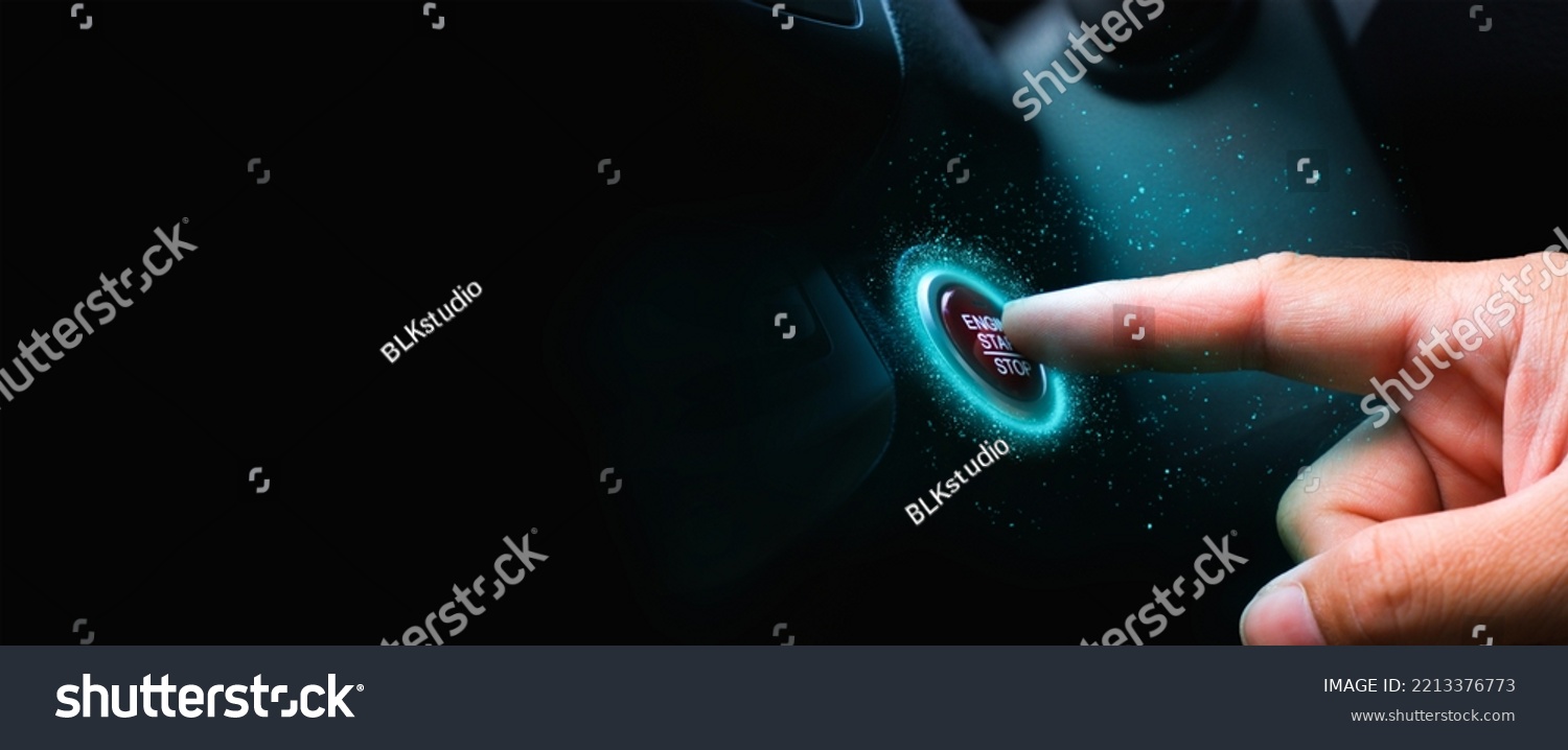 The driver palm as it presses the electric car engine start stop button with a blue light illuminated , panoramic banner with copy space on black background #2213376773