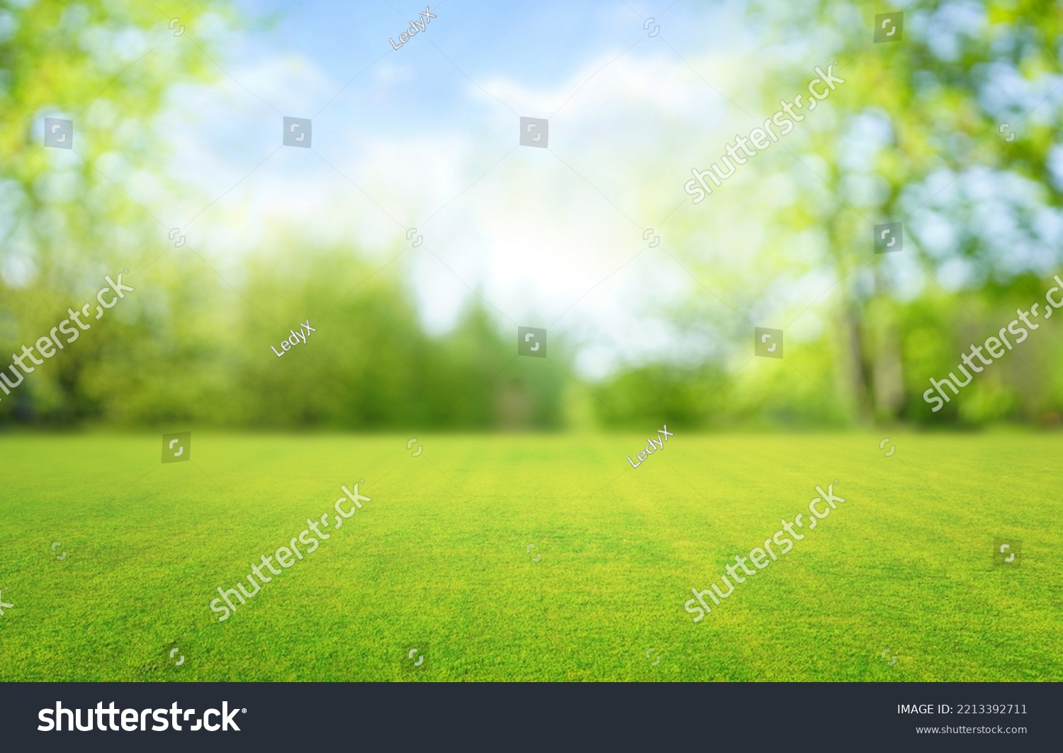 Beautiful blurred background image of spring nature with a neatly trimmed lawn surrounded by trees against a blue sky with clouds on a bright sunny day. #2213392711