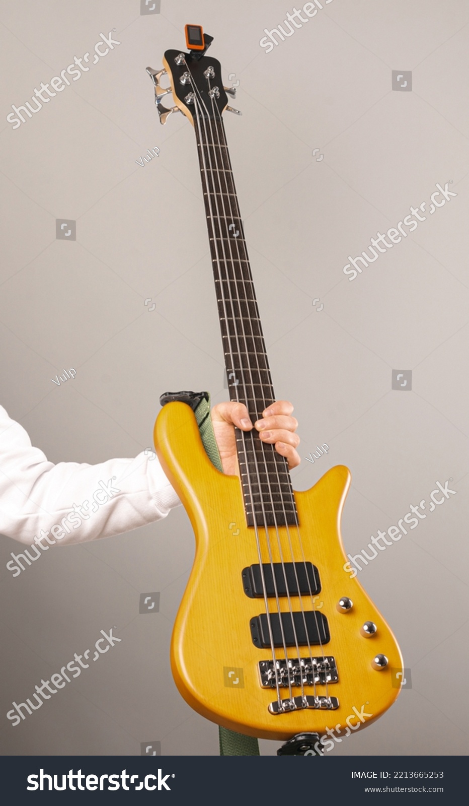 Vertical shot of a strong man hand holding a bass guitar with five chords. Studio shot over light grey background. #2213665253