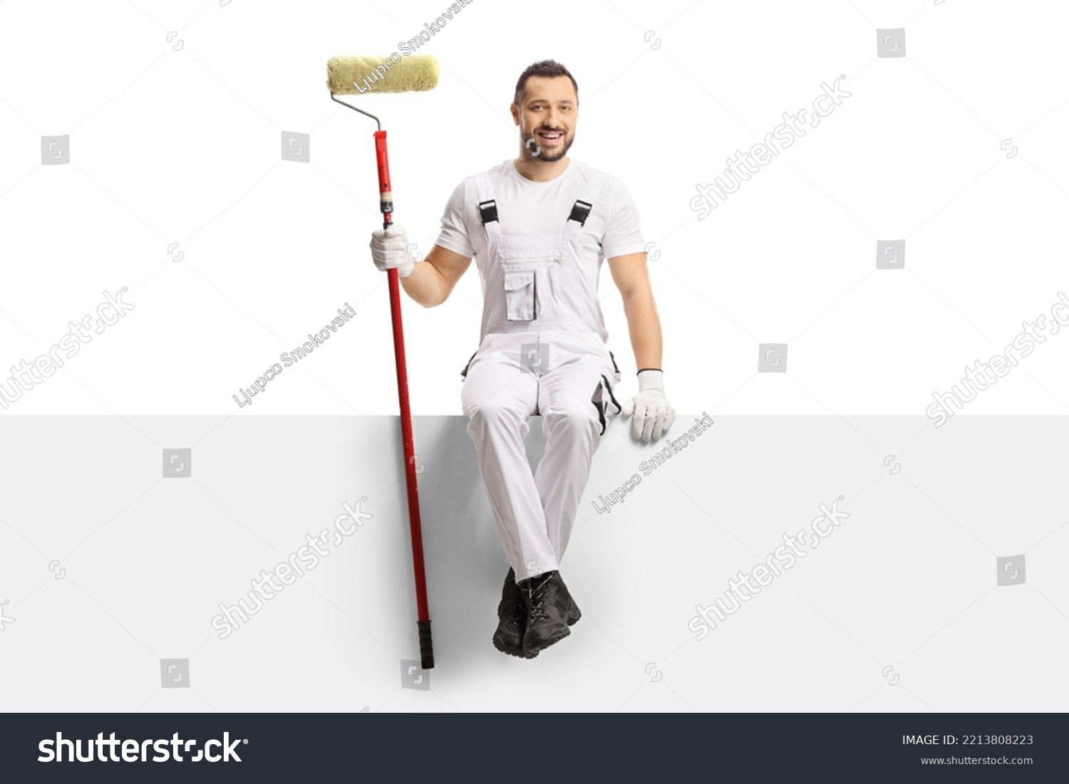 Painter holding a paint roller and sitting on a blank panel isolated on white background #2213808223