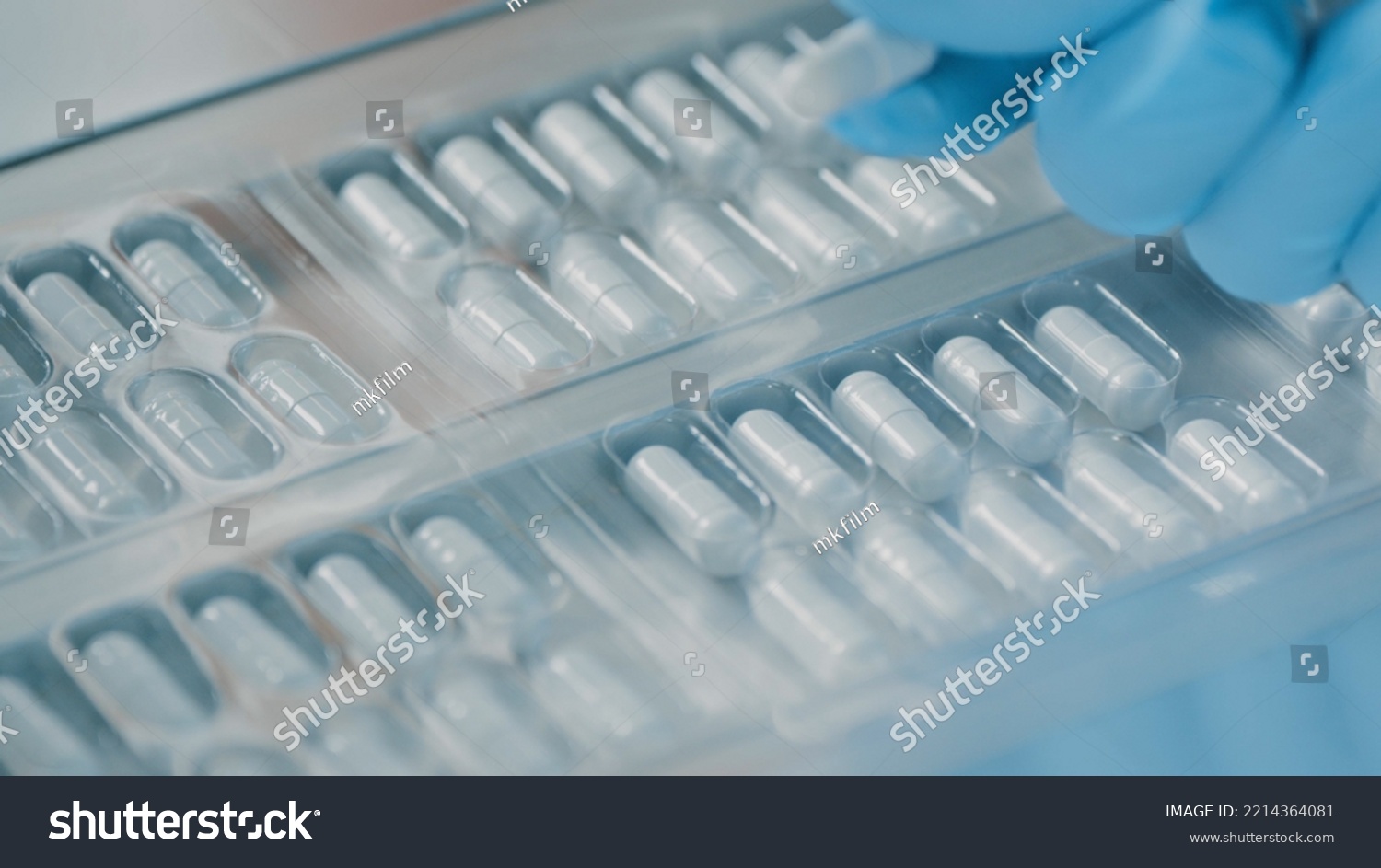 Pharmacologist checks blister packs with medicinal capsules moving on a conveyor. Plastic package with capsule meds. Medication capsules in blisters. Pharmaceutical factory production line. Macro #2214364081