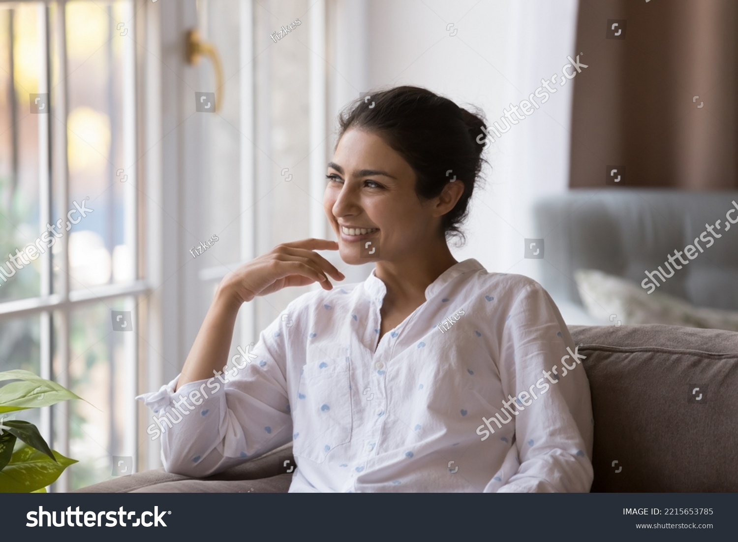 Young millennial dreamy Indian woman smile staring into distance while relaxing on cozy couch at modern home, enjoy daydreams and carefree weekend leisure feels happy, spend free time alone indoors #2215653785