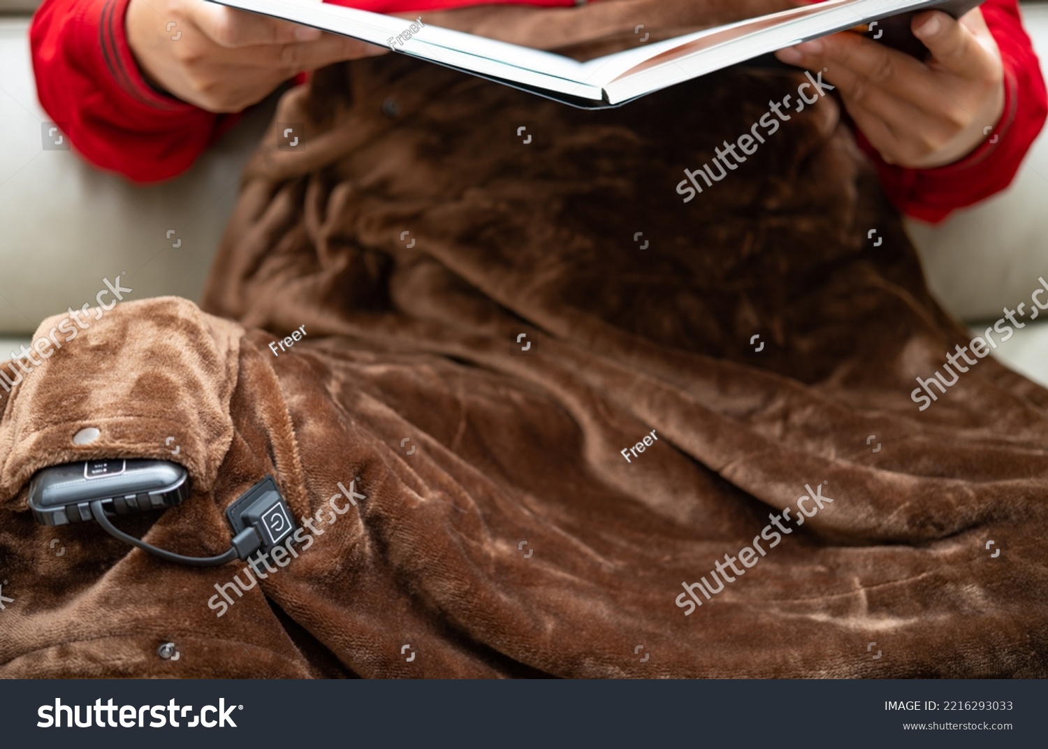man with an electric blanket and reading a book on a sofa #2216293033