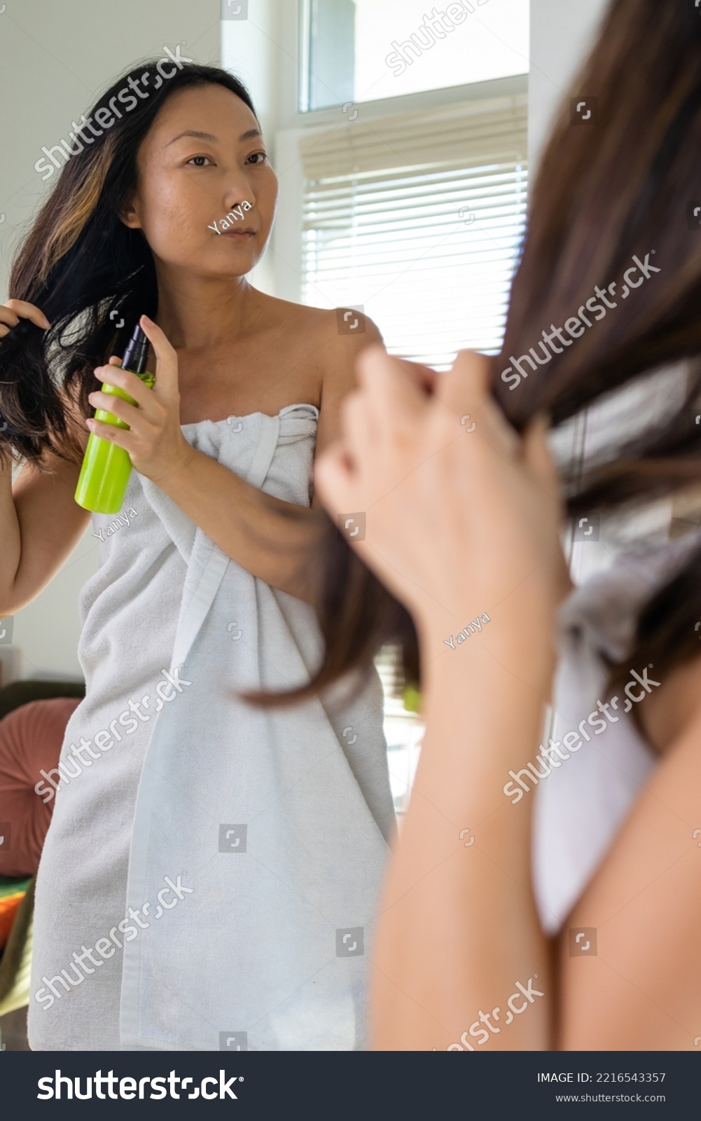 Haircare. Smiling Asian Woman Applying Hair Spray To Split Ends, Young Happy Female Standing Wrapped In Towel After Shower Using avocado conditioner At Home. #2216543357