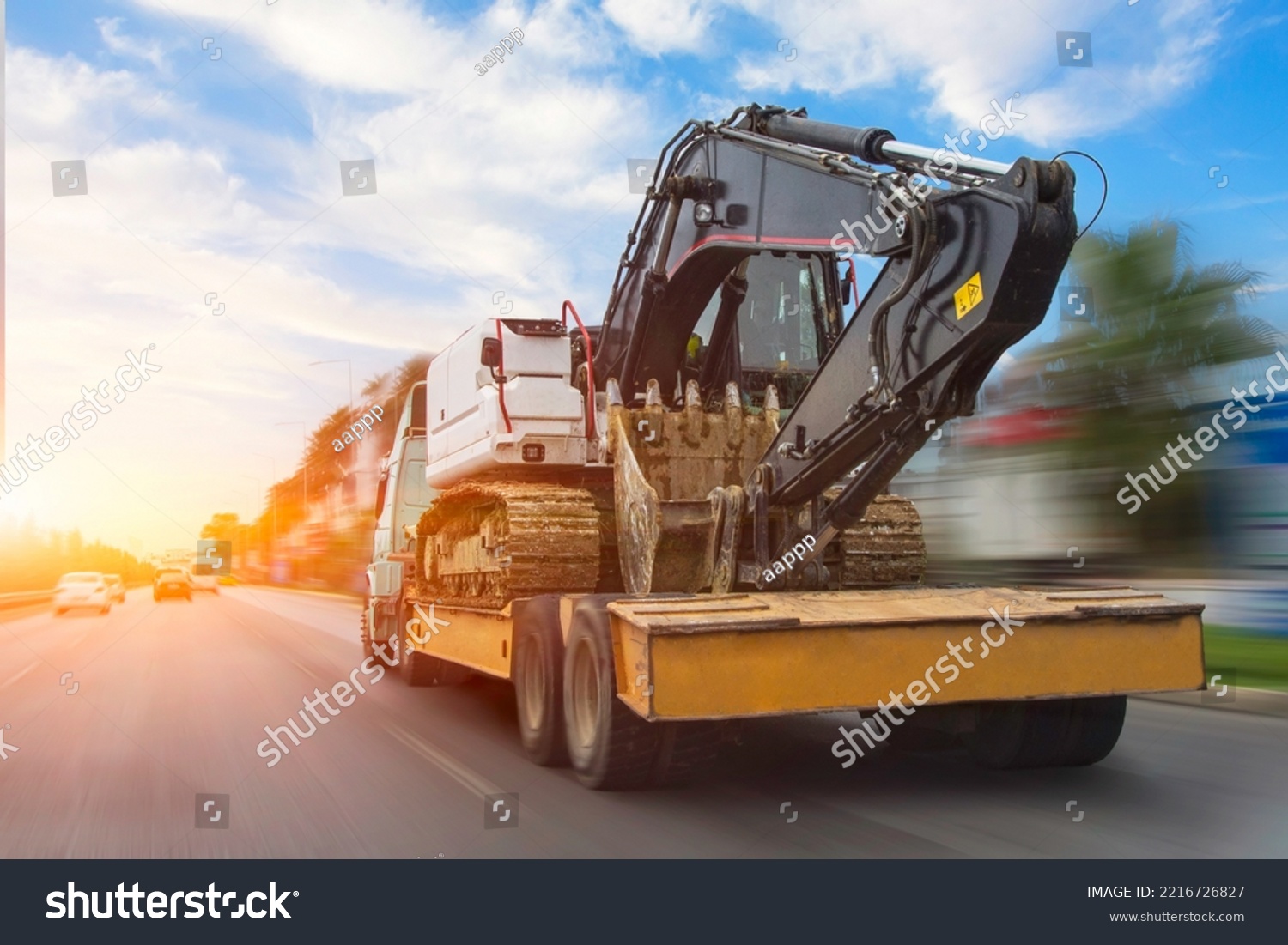 Transportation of a dirty excavator on a truck trailer after its work. Motion speed and blur effect on city highway, during sunset sky #2216726827