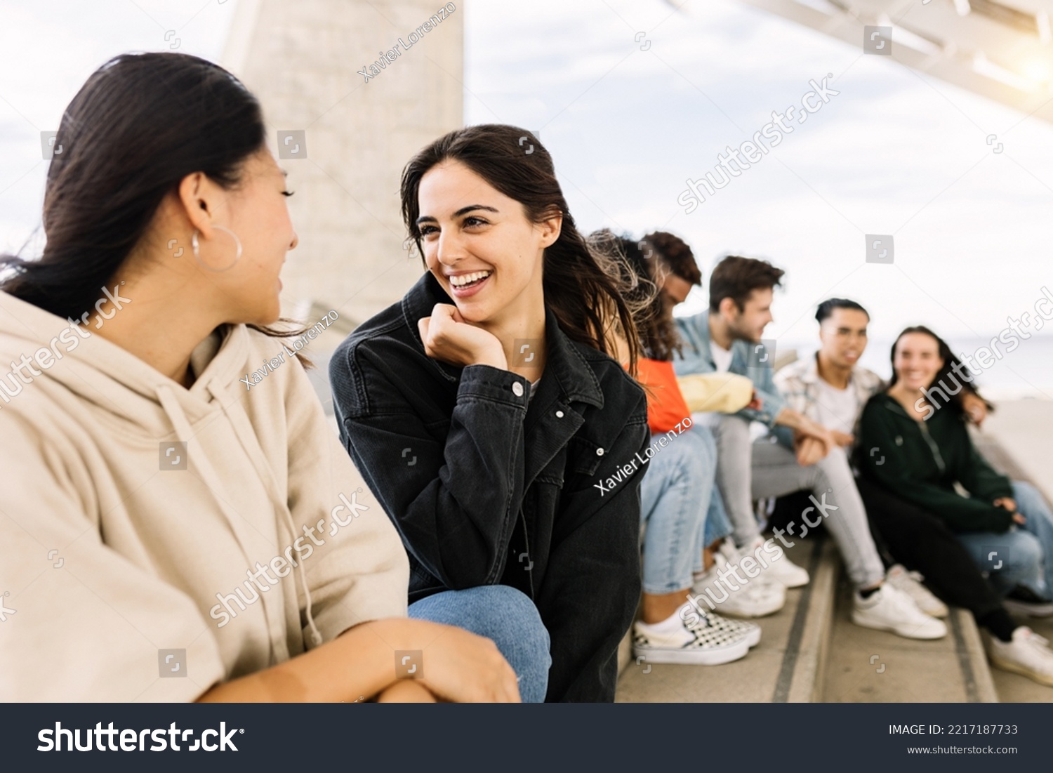 Happy young group of multiracial friends hanging out together outdoors - Millennial diverse people social gathering relaxing in city street - Focus on pretty caucasian woman #2217187733