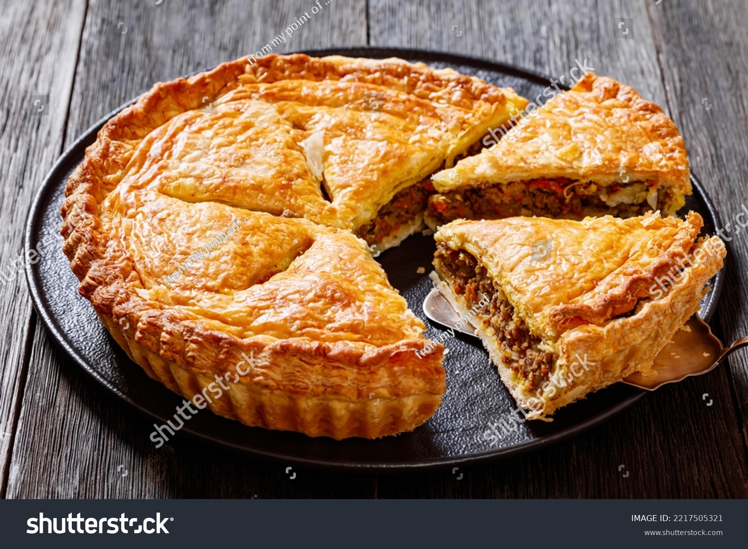 sliced Ground Beef Meat Pie with a flaky puff pastry double crust with hearty minced beef cooked with vegetables and seasoning on black plate on wood table #2217505321