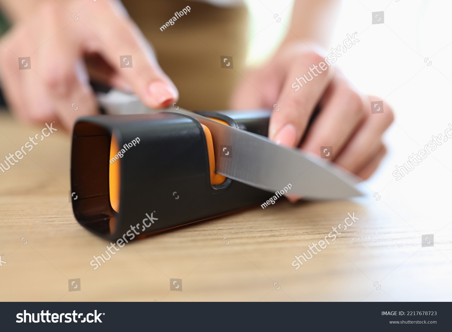 Close-up of woman sharpening knife with special knife sharpener. Grindstone, kitchen tools and devices concept #2217678723