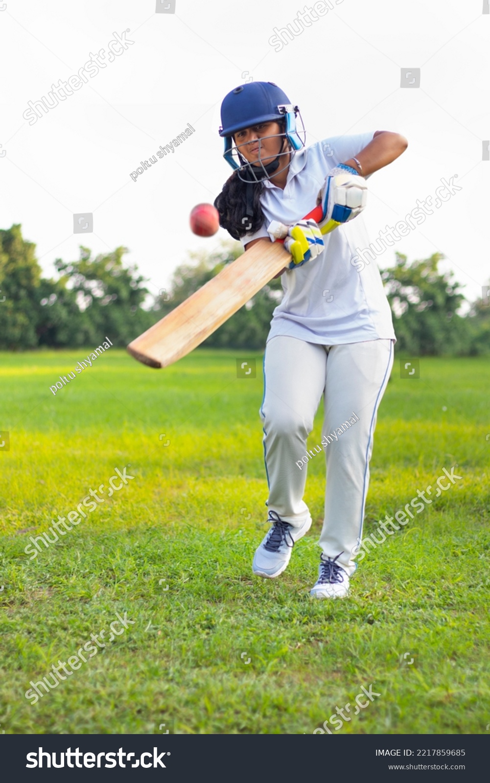 Female Indian cricket player wearing protective gear and hitting the ball with a bat on the field #2217859685