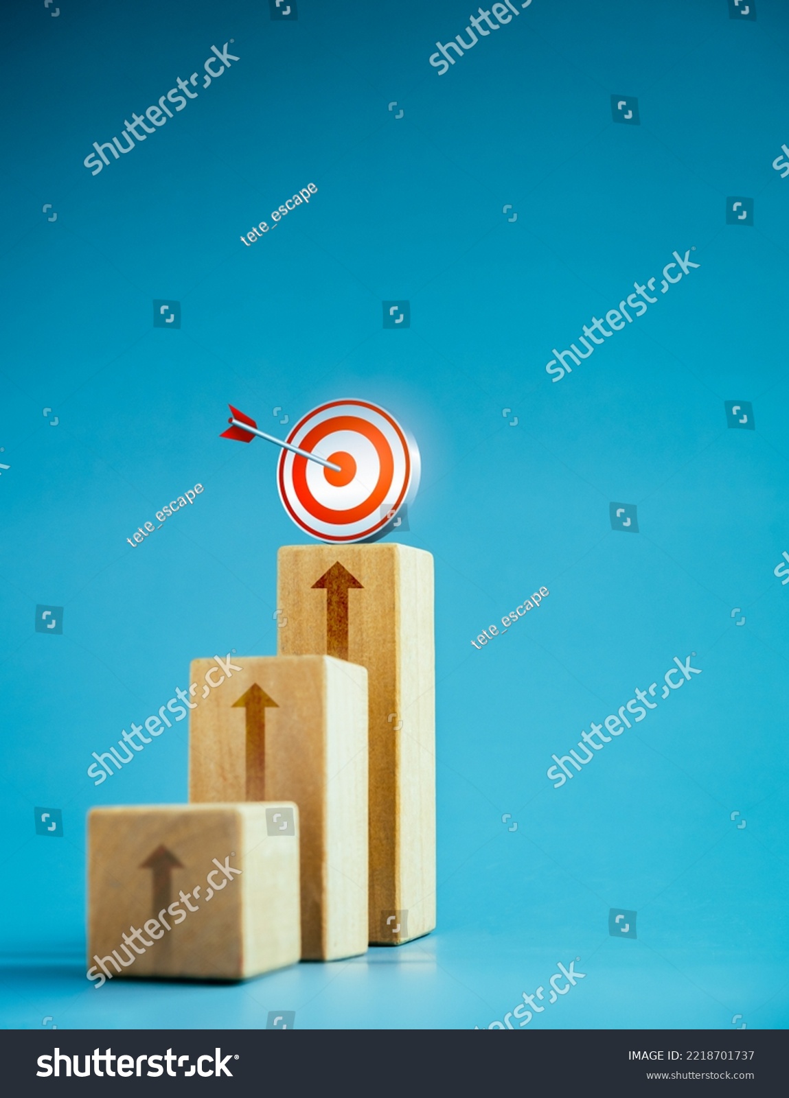 Target icon on top of wooden blocks with rise up arrows, 3d bar graph chart steps on blue background, vertical style, business growth process, profit, investment, economic improvement concepts. #2218701737