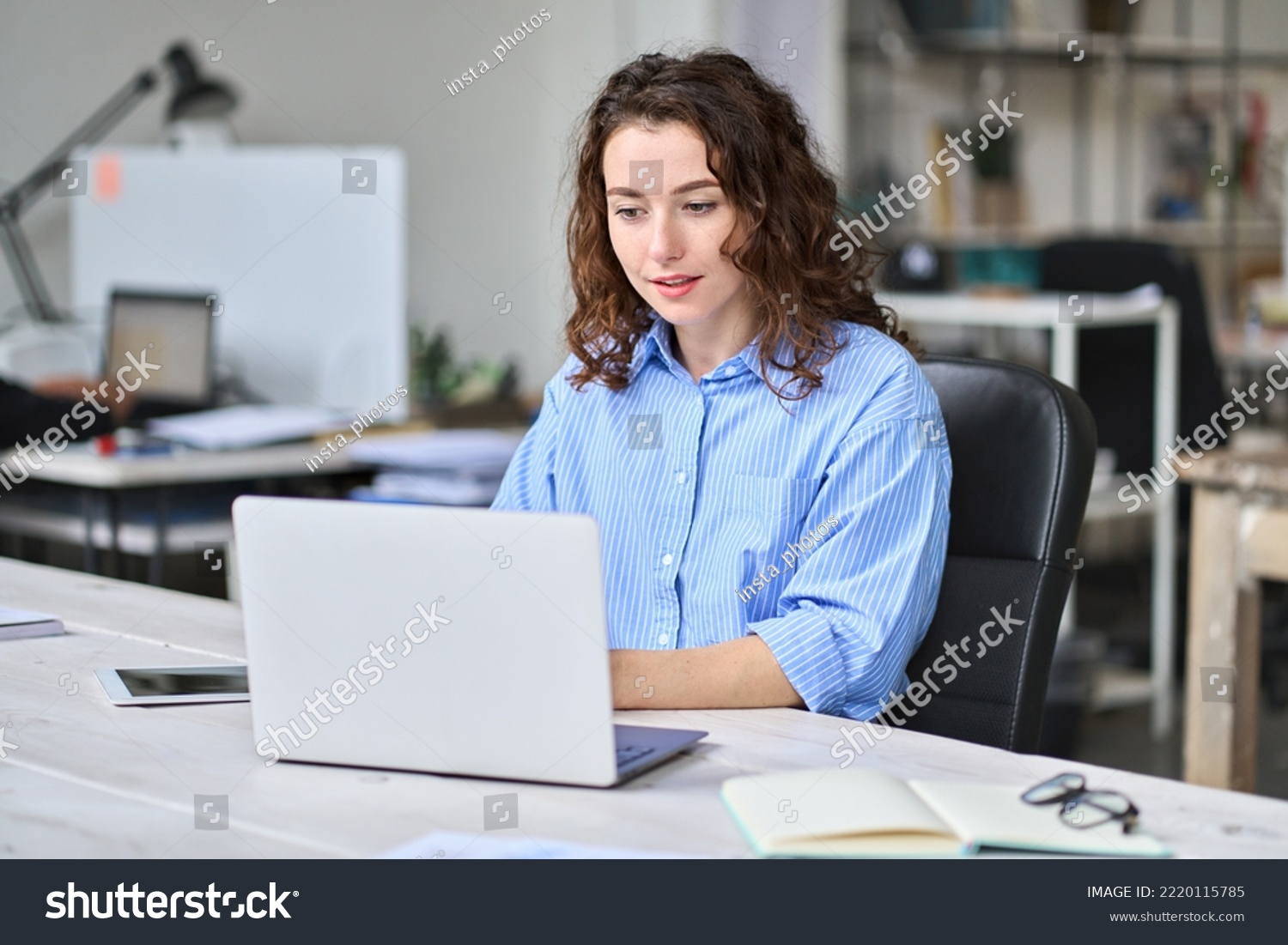Young business woman company employee sitting at desk working on laptop. Busy female professional worker marketer using computer in corporate modern office managing data technology operations. #2220115785