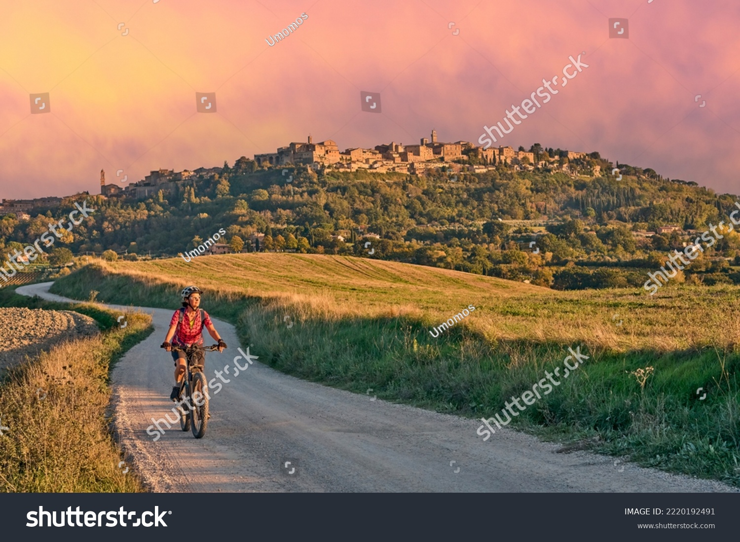 nice senior woman riding her electric mountain bike between olive trees in the Ghianti area with Montepulciano in background, Tuscany , Italy #2220192491