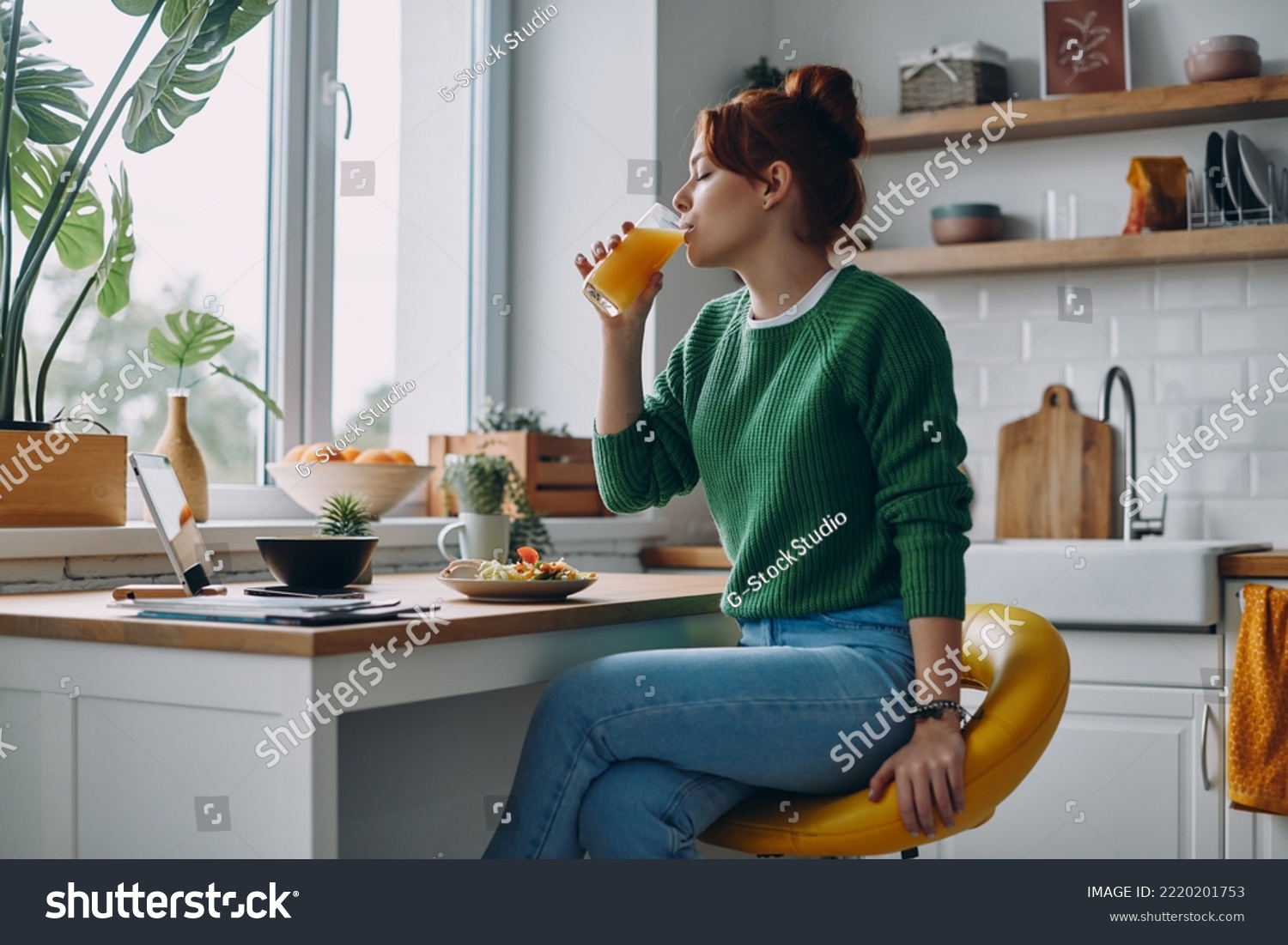 Beautiful redhead woman drinking juice while having lunch at the domestic kitchen #2220201753