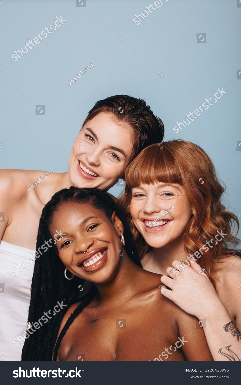 Happy women with different skin tones smiling at the camera in a studio. Group of body confident young women embracing their natural beauty. Three body positive young women standing together. #2220423995