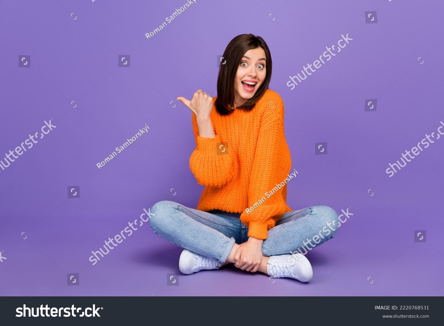 Full size photo of lovely young woman sit floor point copyspace dressed stylish orange knitted look isolated on purple color background #2220768531