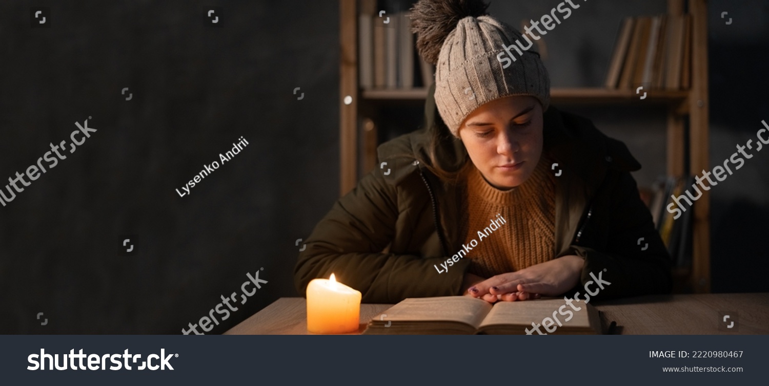 Young woman with warm clothing feeling the cold inside house, dark home no electricity, student studying using candlelight. Concept of no heating and no power in winter at home. Banner #2220980467