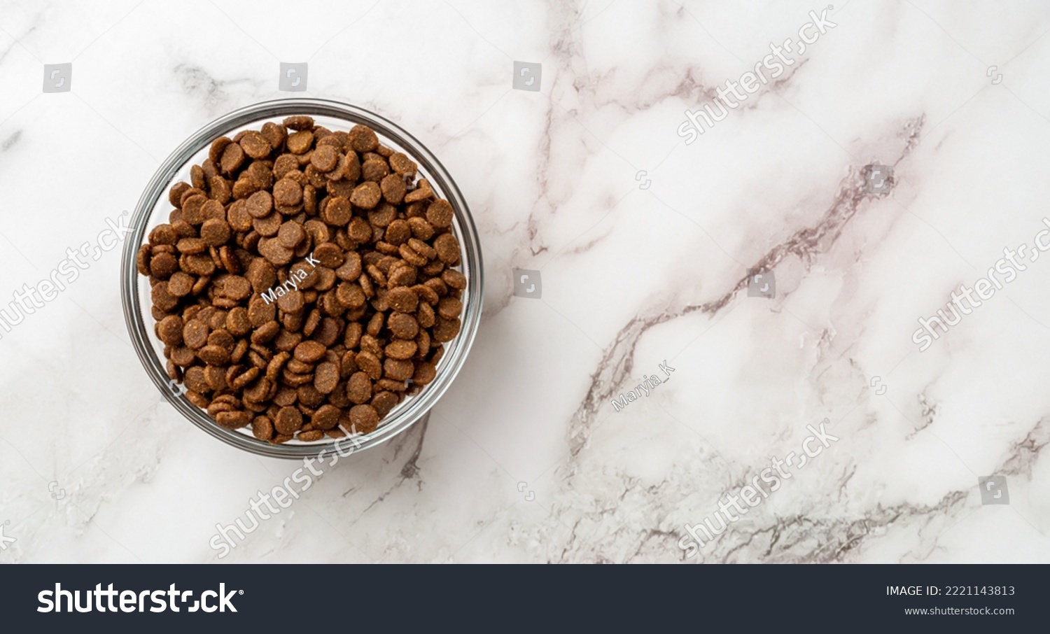 Dry pet food in a glass bowl over marble background. Glass feeding bowl full of gluten free dry protein kibbles for cats closeup. Complete food for domestic animals concept. Copy space. Top view. #2221143813