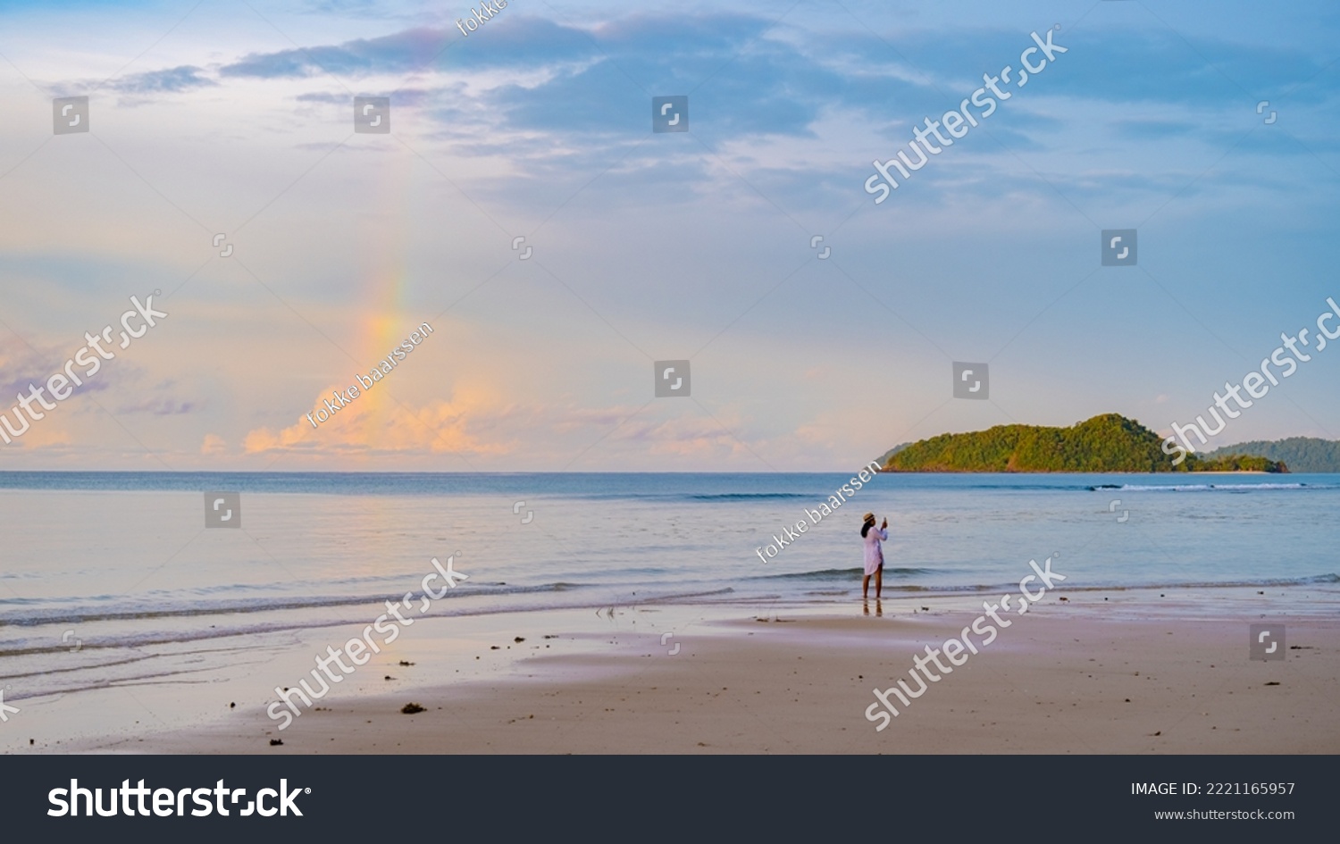 Asian women looking at a rainbow on the beach after a monsoon rain storm in Thailand.Asian women walking on the beach of Koh Mak during sunrise #2221165957