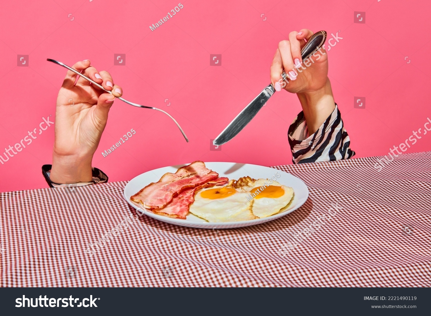 Female hands with fork and knife eating English breakfast with fried eggs and bacon . Vintage, retro style interior. Food pop art photography. Complementary colors. Copy space for ad, text #2221490119