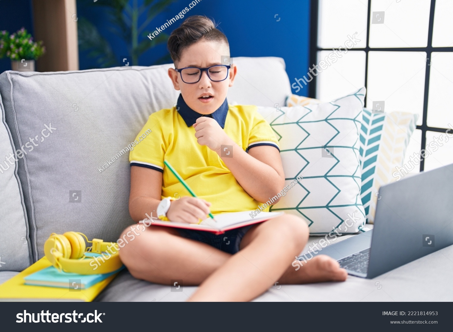 Young hispanic kid doing homework sitting on the sofa feeling unwell and coughing as symptom for cold or bronchitis. health care concept.  #2221814953
