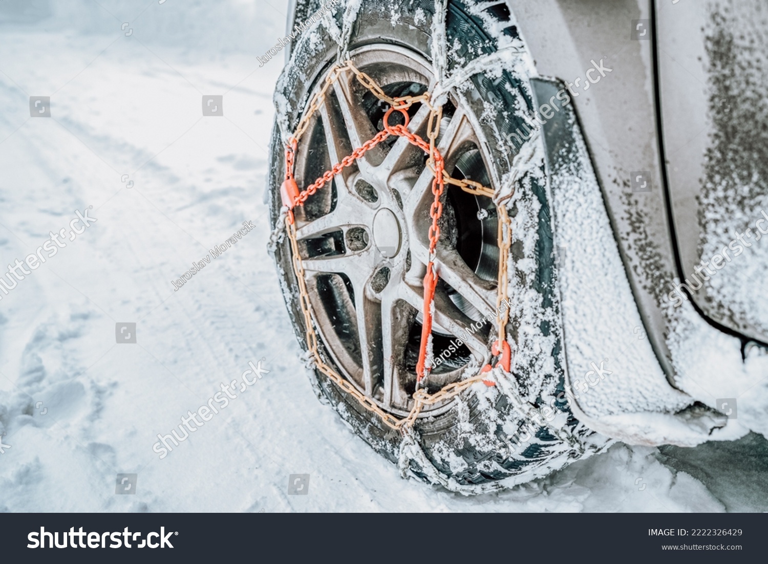 Snow chains on tire. Car wheel with traction chains on a snowy winter road #2222326429