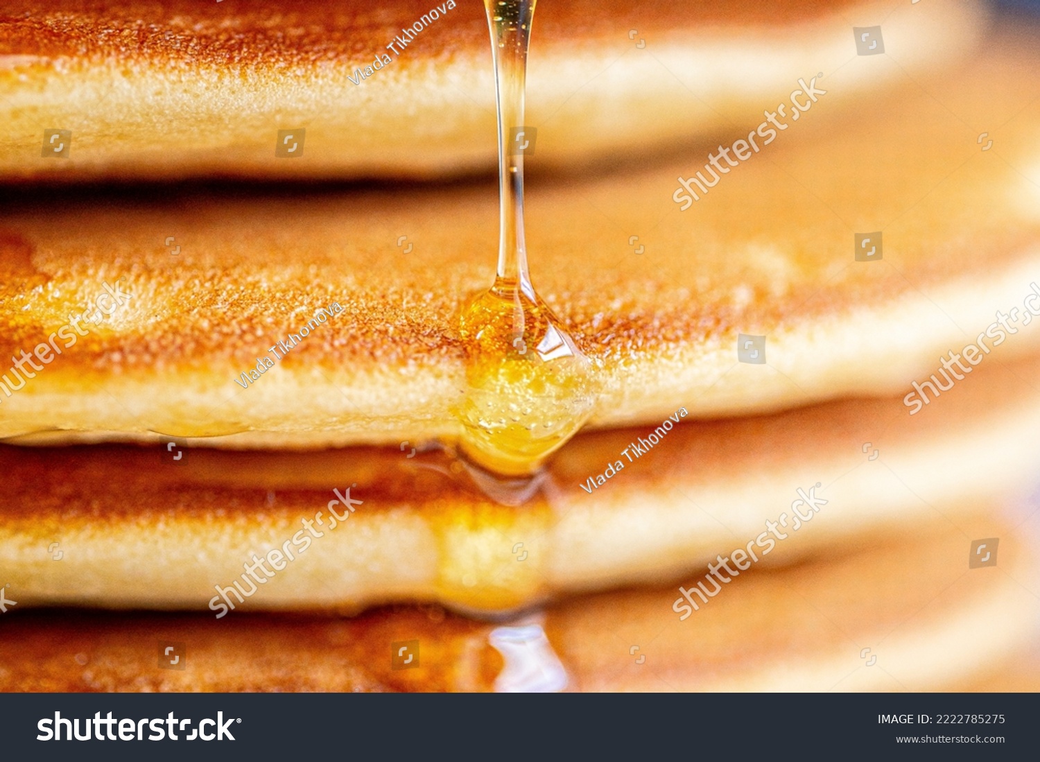 A drop of honey spreads over the pancake.Pancakes with syrup macro shot.Syrup pours on a pancake macro photo.Honey spreads.Drop of syrup close-up.Golden pancakes with glitter syrup.Delicious sweet  #2222785275