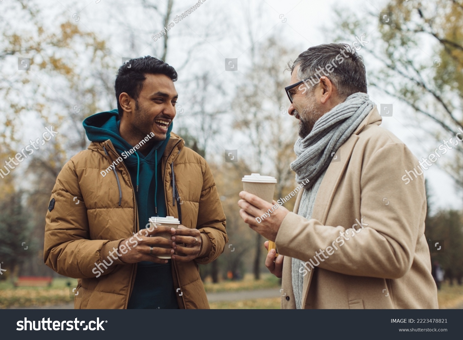 Friends, a senior and a young man walking and talking and drinking coffee together in the autumn park.
 #2223478821
