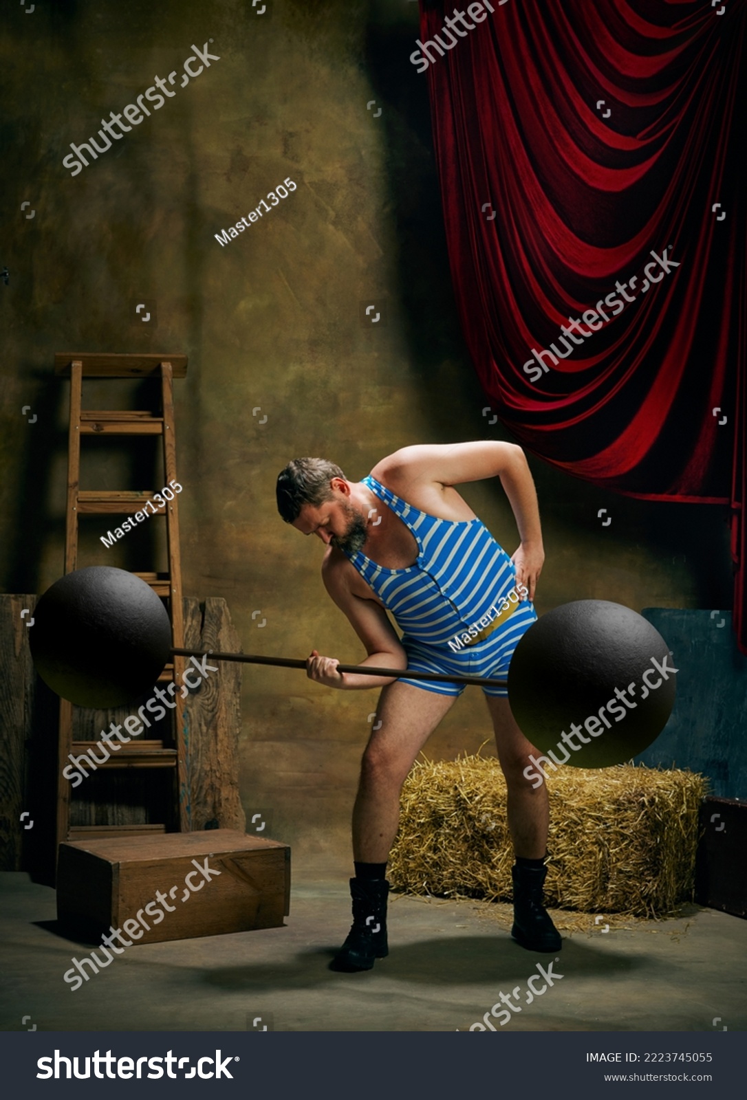 Circus athlete. Vintage portrait of retro circus strongman wearing blue striped sports swimsuit training with barbell over dark circus backstage background. Concept of creative art, fashion, style #2223745055