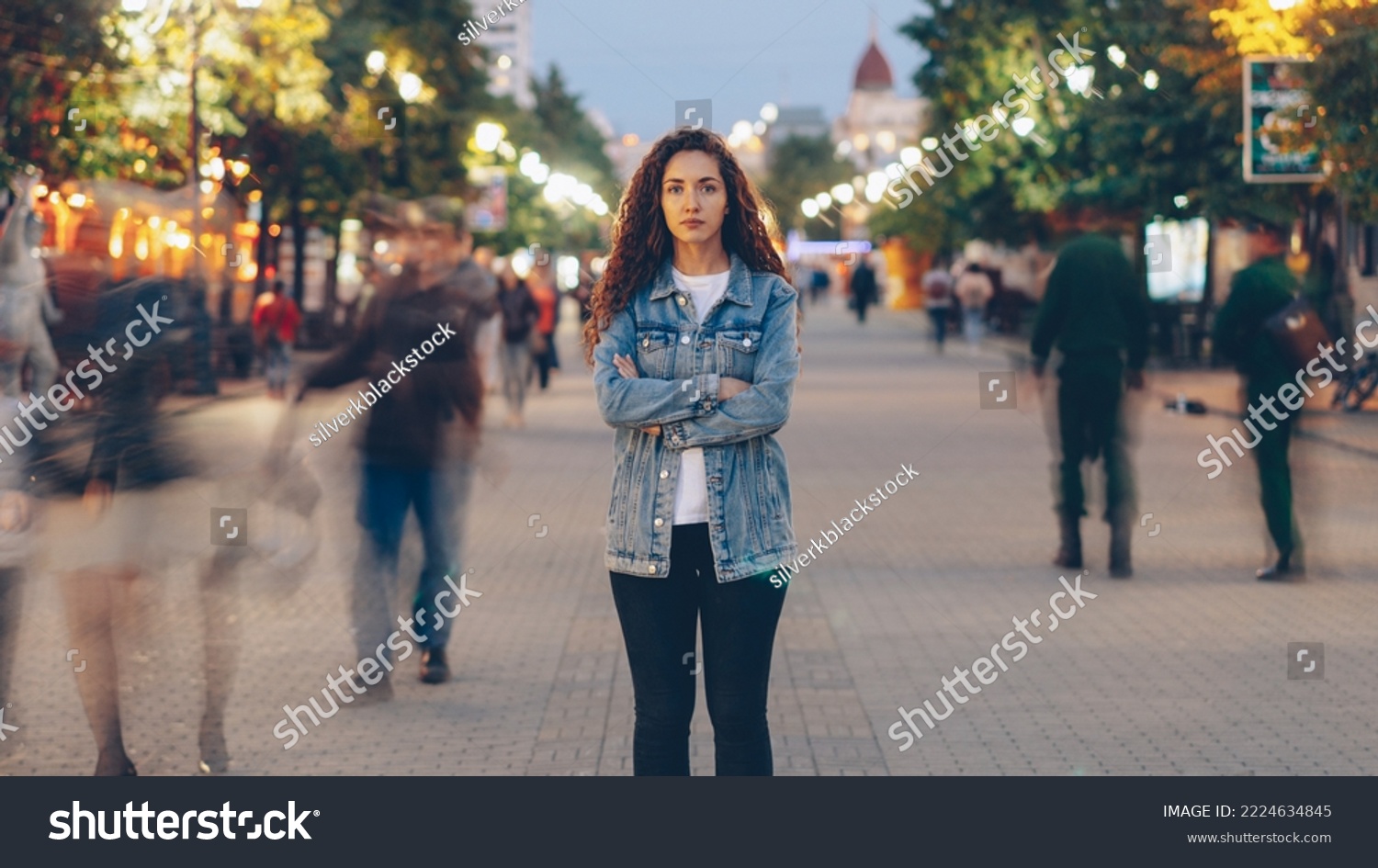 Portrait of stylish young lady tired of usual haste standing in the street among whizzing people and looking at camera. Time, youth and modern society concept. #2224634845