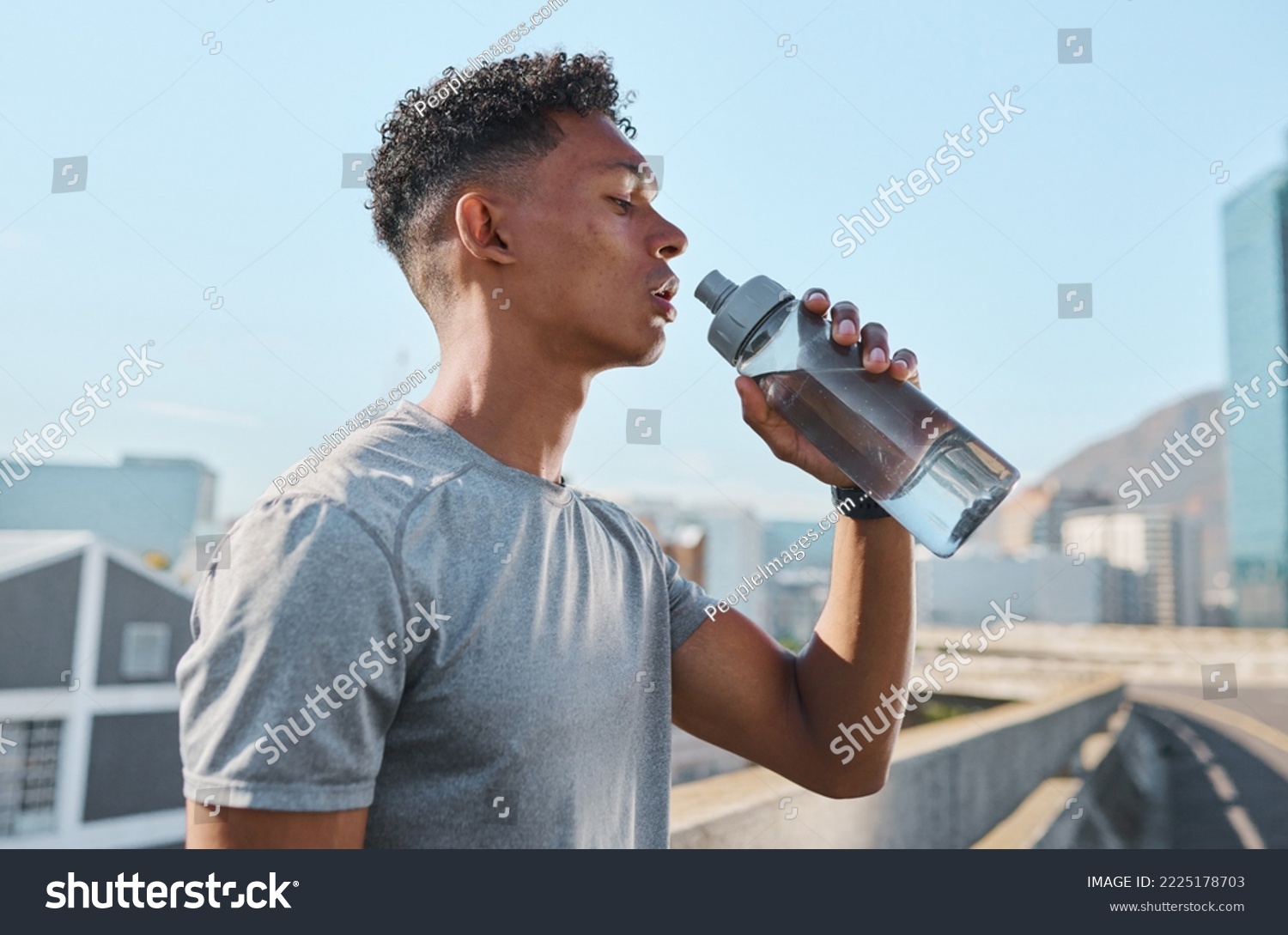 City, fitness and man drinking water after running in street, thirsty after workout in summer heat. Sun, exercise run and sweat, urban black man with healthy lifestyle and water bottle relax on road #2225178703