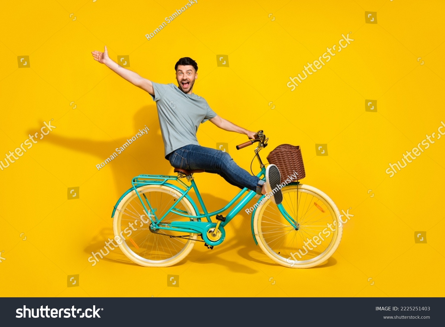 Side profile photo of funky crazy excited man wear gray t-shirt denim jeans sitting new retro bicycle raise palm hello friends isolated on yellow color background #2225251403