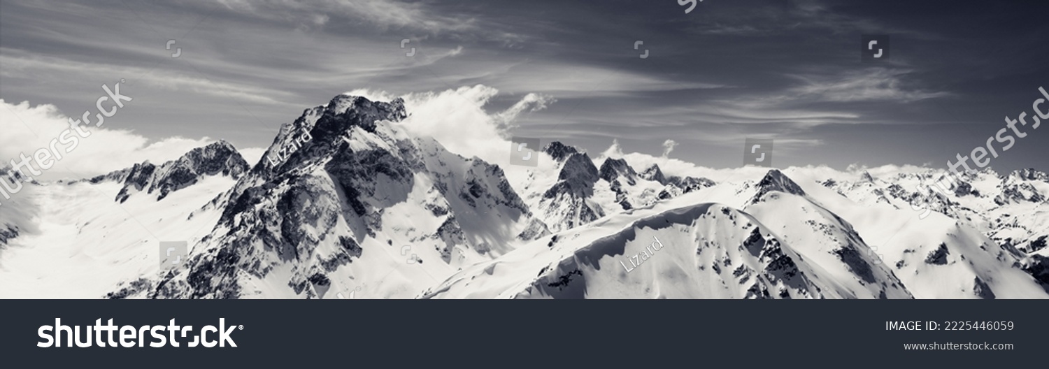 Black and white panorama of high snow-capped mountain peaks and beautiful sky with clouds at sun windy day. Caucasus Mountains in winter, region Dombay, mount Dombay-Ulgen. #2225446059