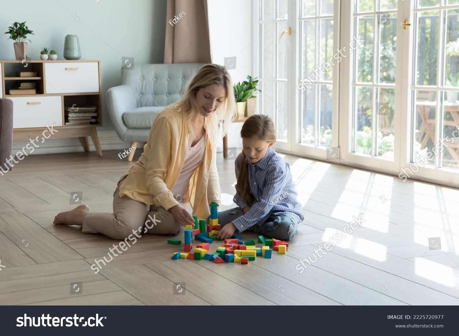 Loving mother play with little 6s daughter at home, using wooden cubes build castle sit together on warm floor in cozy sunny living room. Family pastime and leisure, developmental games with children #2225720977