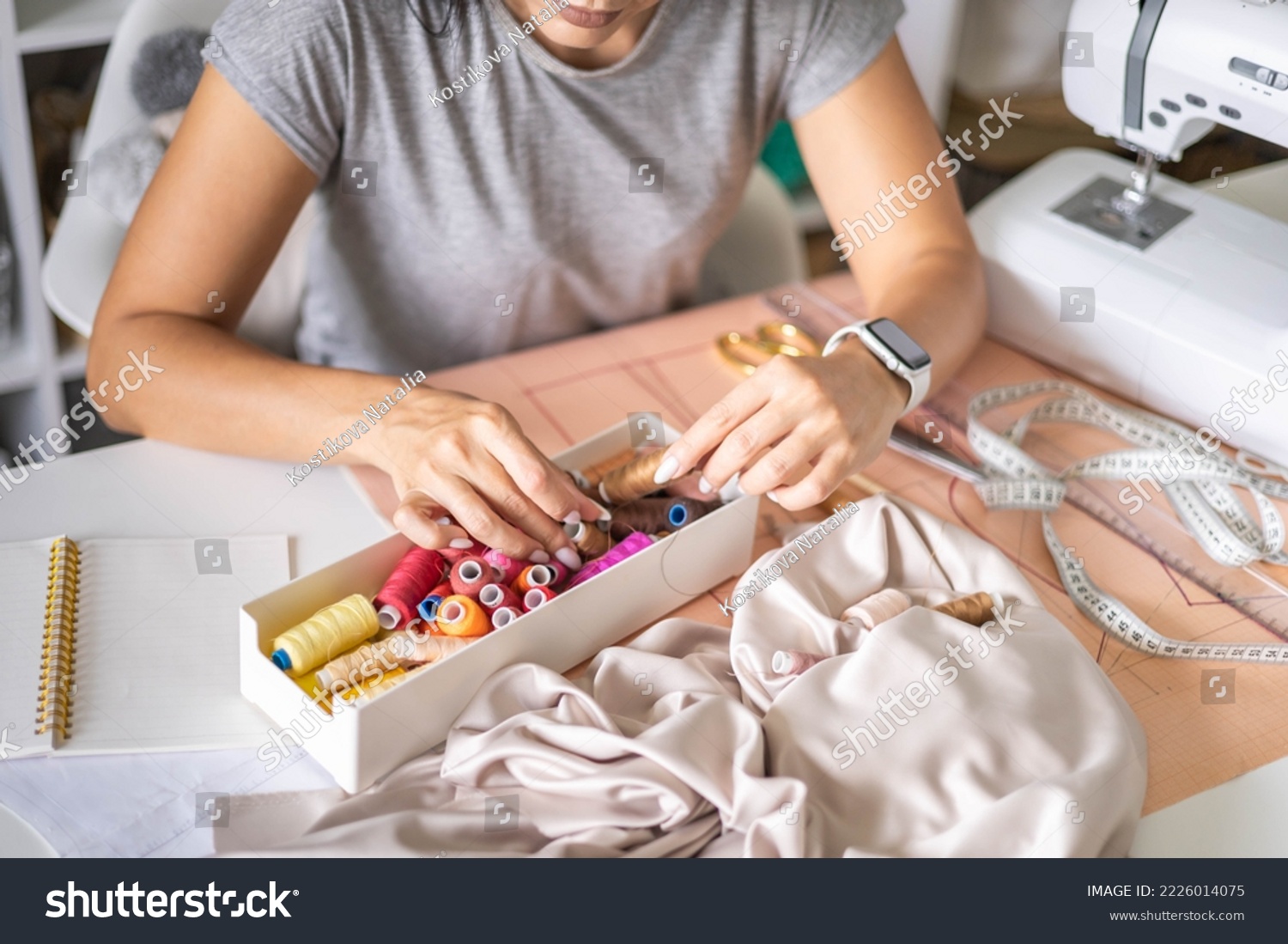 Woman dressmaker hands choosing thread color for sewing beige fabric clothes at workshop studio closeup. Female tailor fashion designer art work modist dressmaking professional occupation top view #2226014075