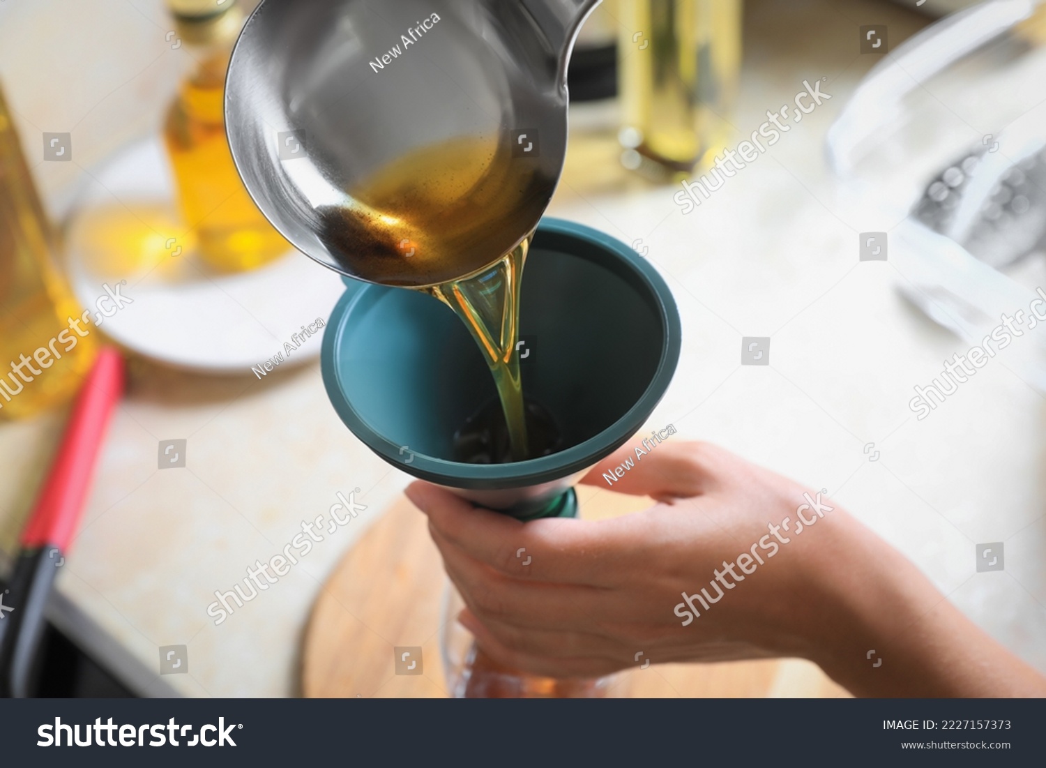 Woman pouring used cooking oil into bottle through funnel in kitchen, closeup #2227157373