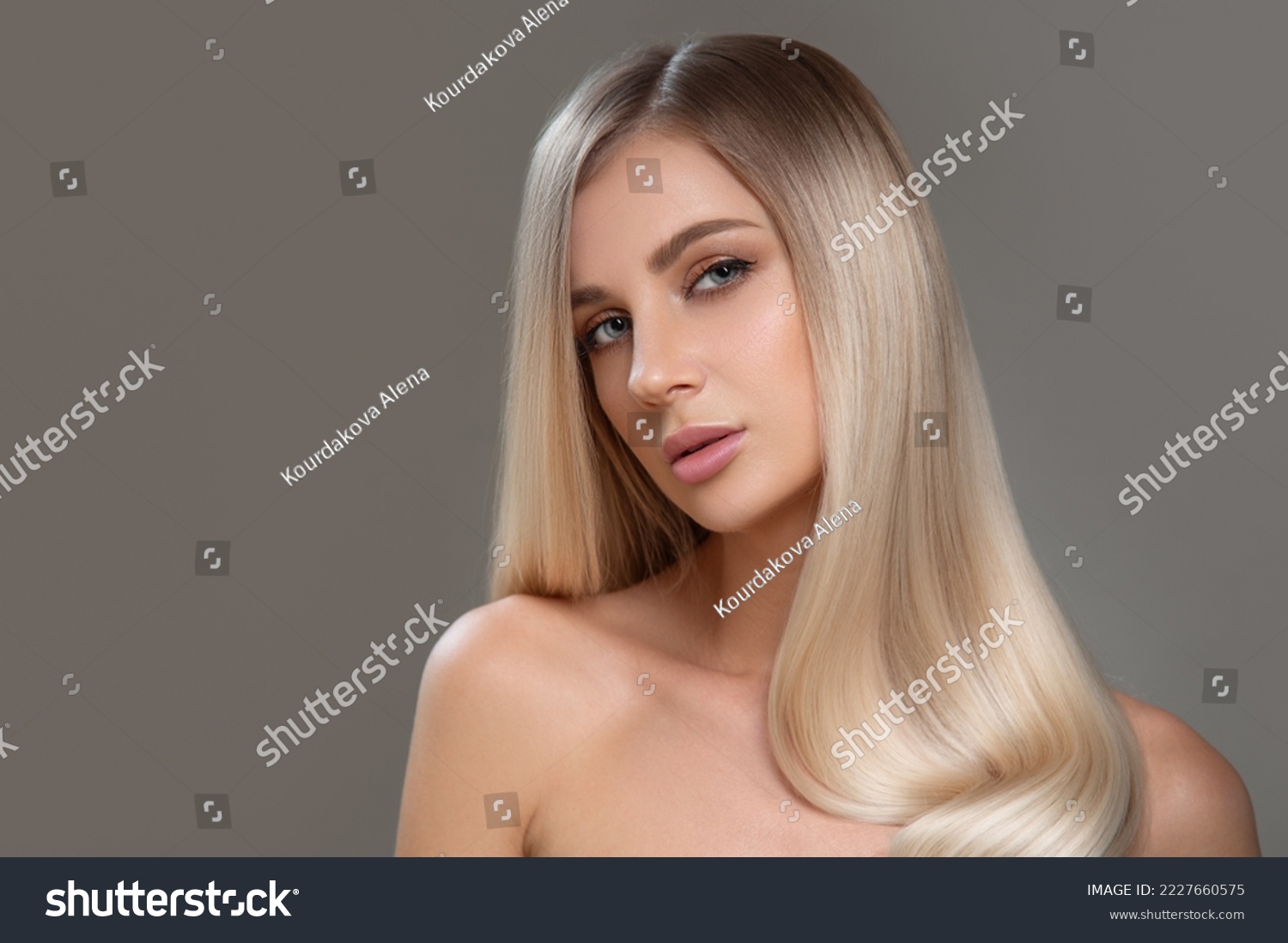 Beautiful young blonde with straight shiny hair. Portrait on a gray background. Hair and makeup #2227660575