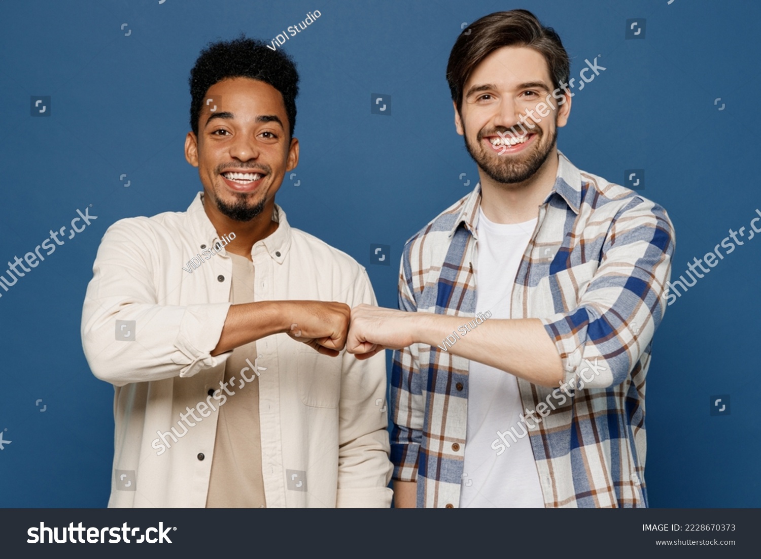 Young two friends cheerful cool smiling men 20s wear white casual shirts looking camera together give fistbump isolated plain dark royal navy blue background studio portrait. People lifestyle concept #2228670373