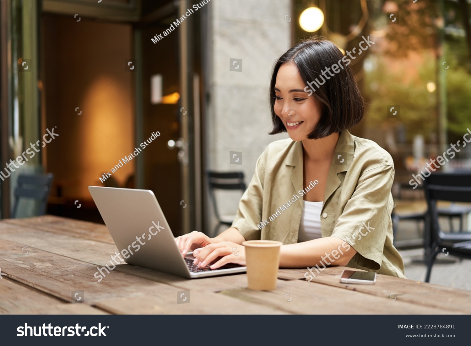 Young asian woman, digital nomad working remotely from a cafe, drinking coffee and using laptop, smiling. #2228784891