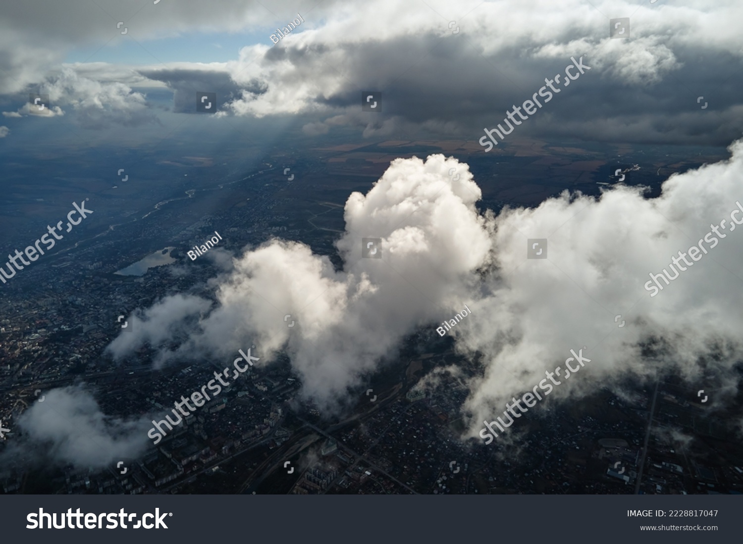 Aerial view from airplane window at high altitude of distant city covered with puffy cumulus clouds forming before rainstorm #2228817047