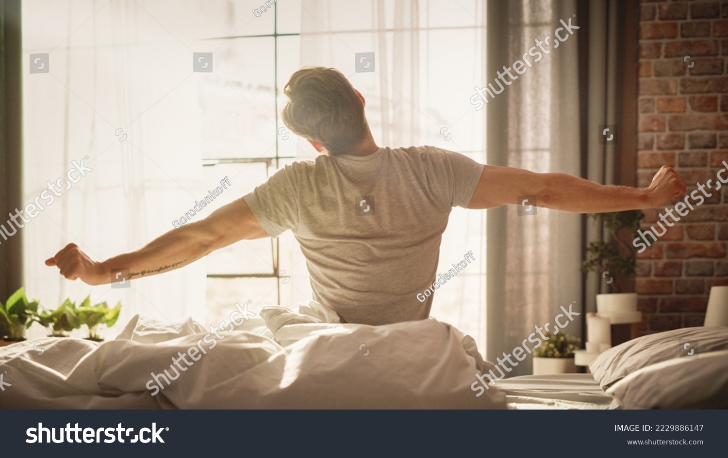 Handsome Young Man Waking up in the Morning, Stretches and Gets Out of Bed, Sun Shines From the Apartment Window in Bedroom, He is Ready for Business Opportunities, Achievements, Adventures #2229886147