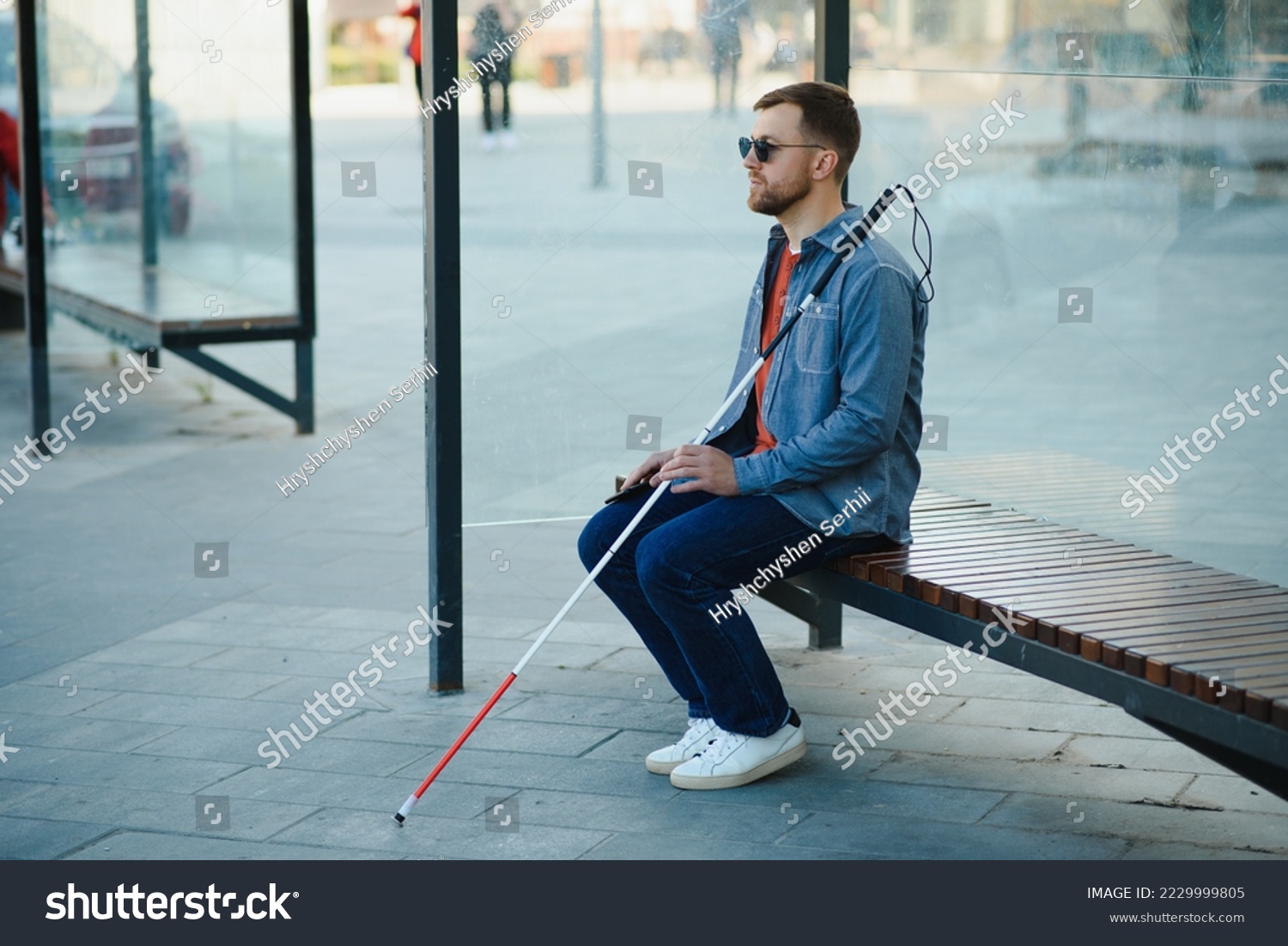 Visually impaired man with walking stick, sitting on bench in city park. Copy space. #2229999805