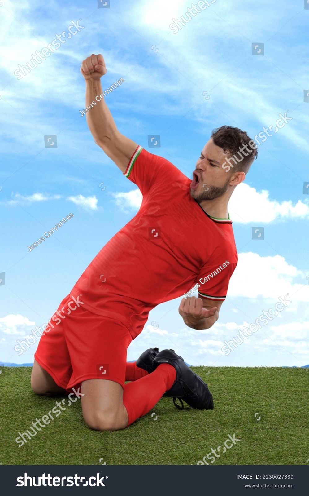 Professional soccer player with a red IR IRAN national team jersey shouting with excitement for scoring a goal with an expression of challenge and happiness on field grass and cloud background #2230027389