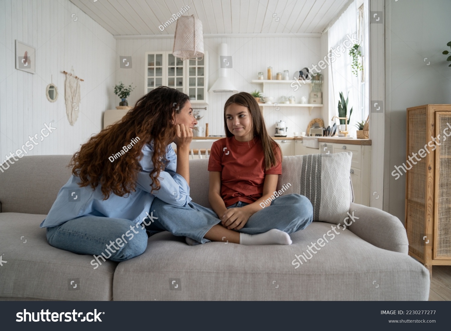 Teenage daughter sharing secrets with young loving supportive mother, parent mom talking chatting with adolescent girl while sitting together on sofa at home. Healthy parent-teen relationships #2230277277